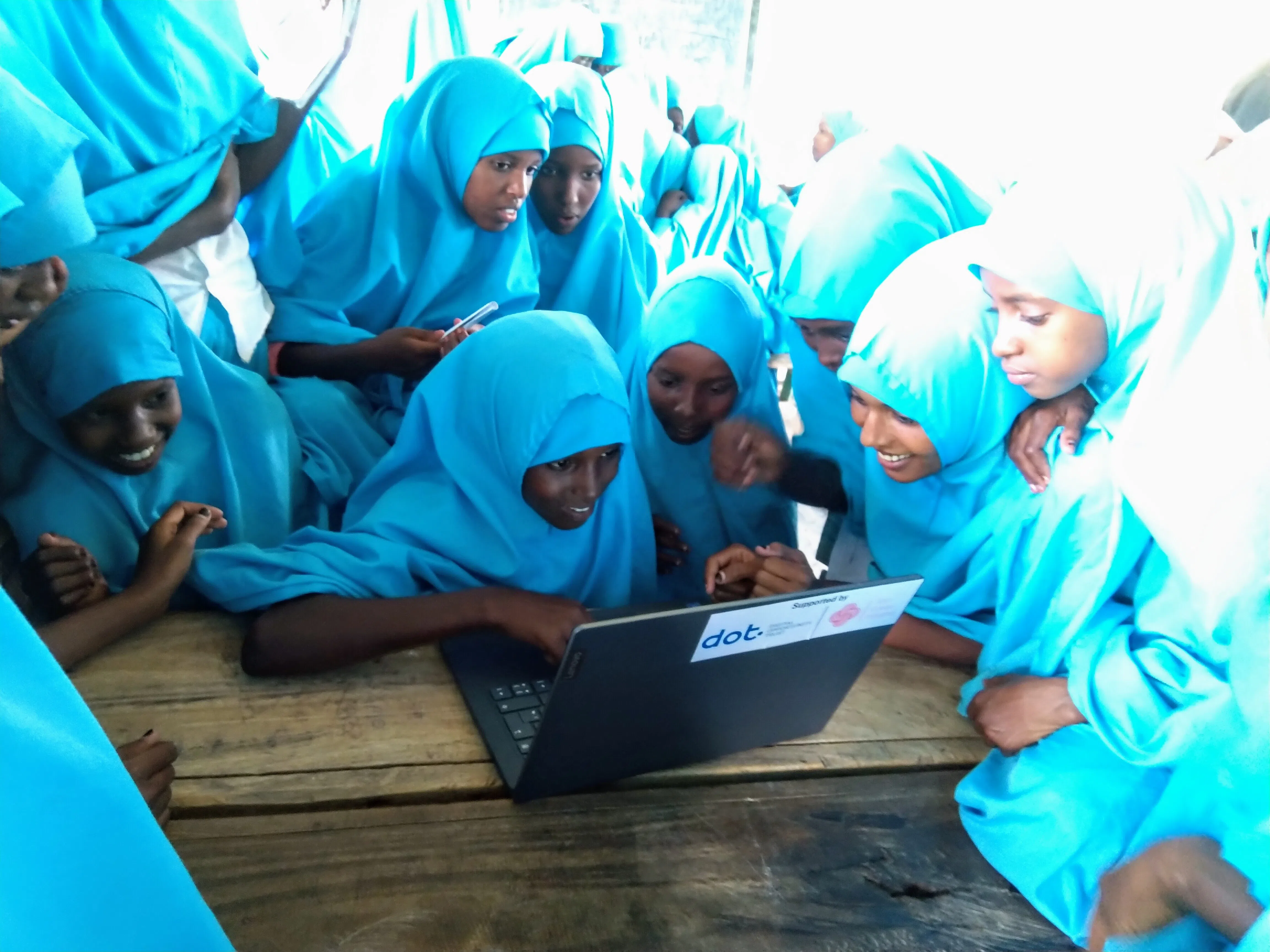 A group of kenyan muslim girls gathered around a laptop