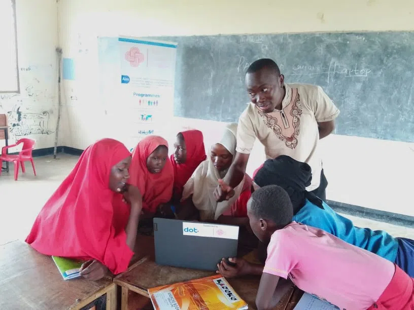 A group of Kenyan muslim girls gathered around a laptop with their teacher teching them