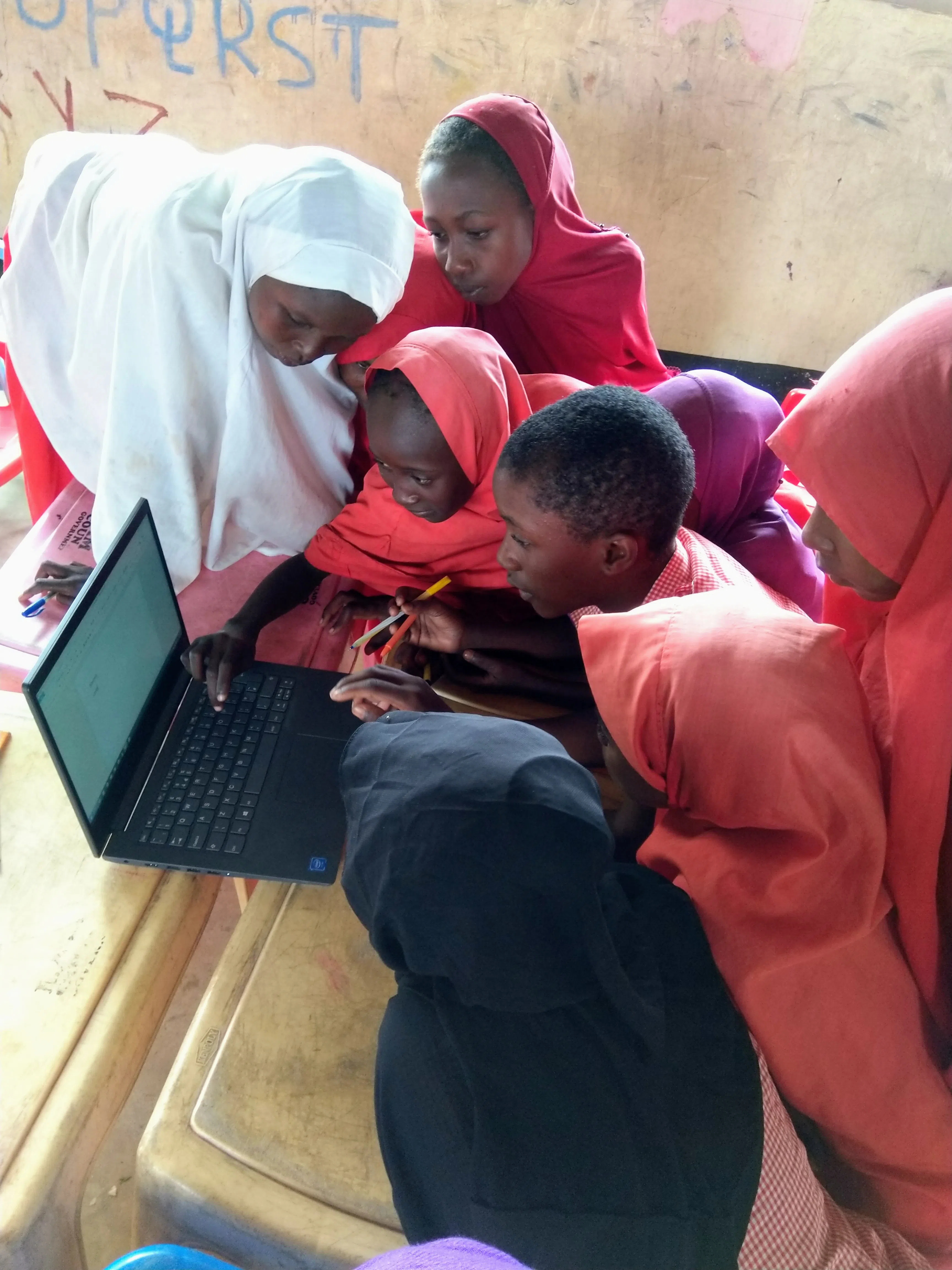 A group of kenyan girls learning ICT gathered around one computer